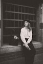 A black and white photo of a woman sitting on a window sill