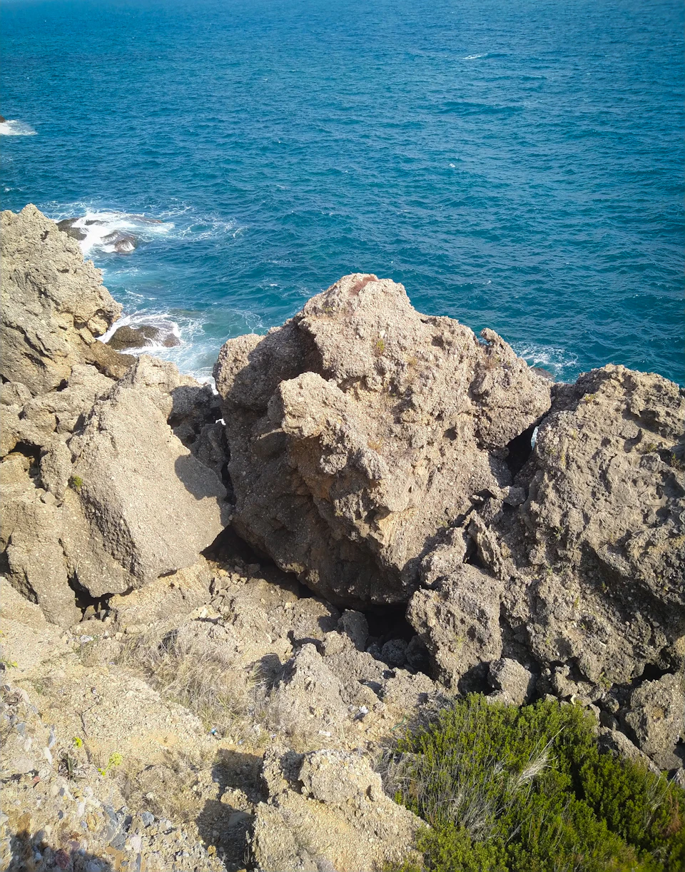 Rocky cliff overlooking ocean with large rock formation and scattered smaller rocks in foreground
