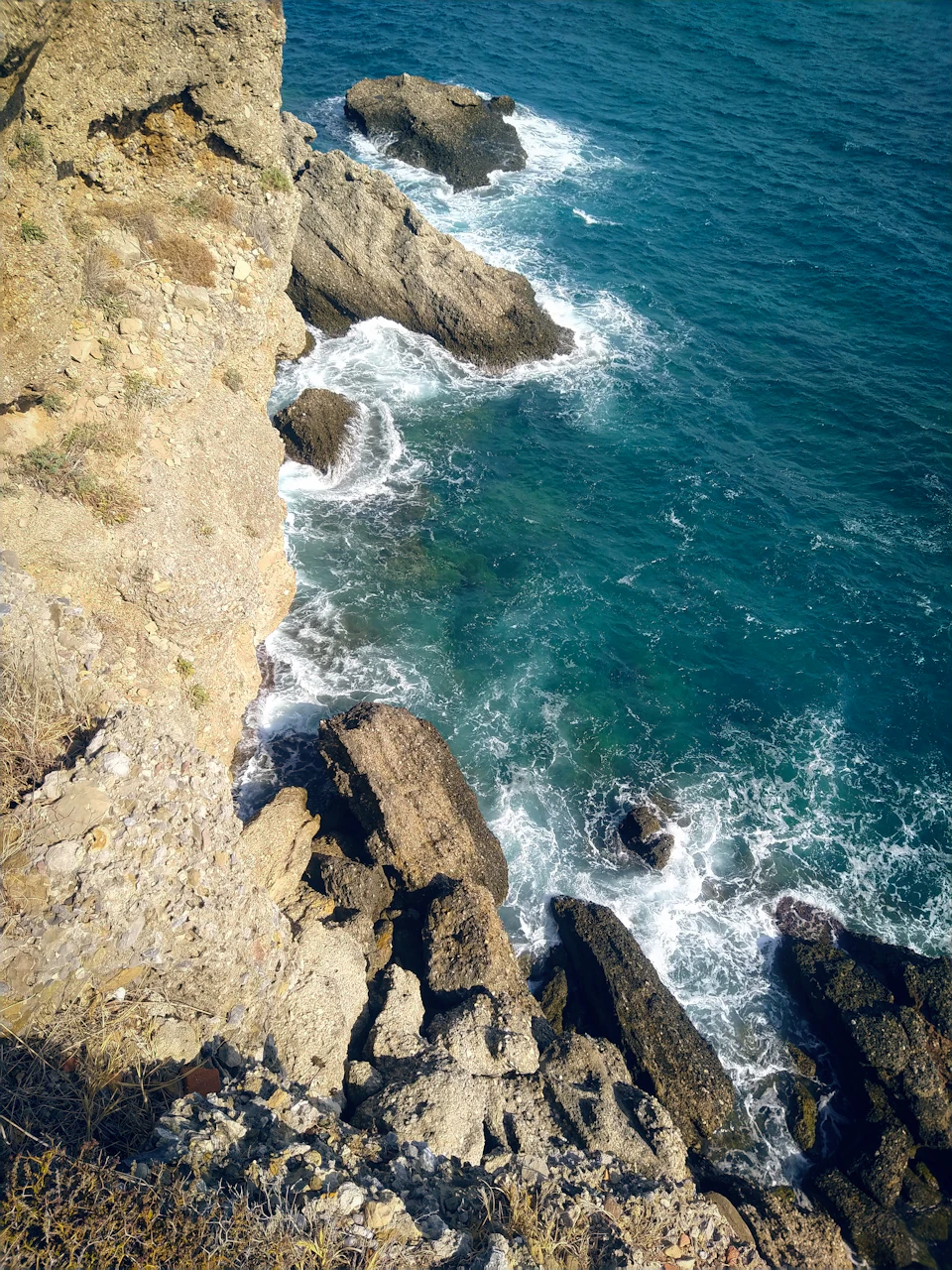 Rocky cliff overlooking ocean with crashing waves against the shore from above perspective