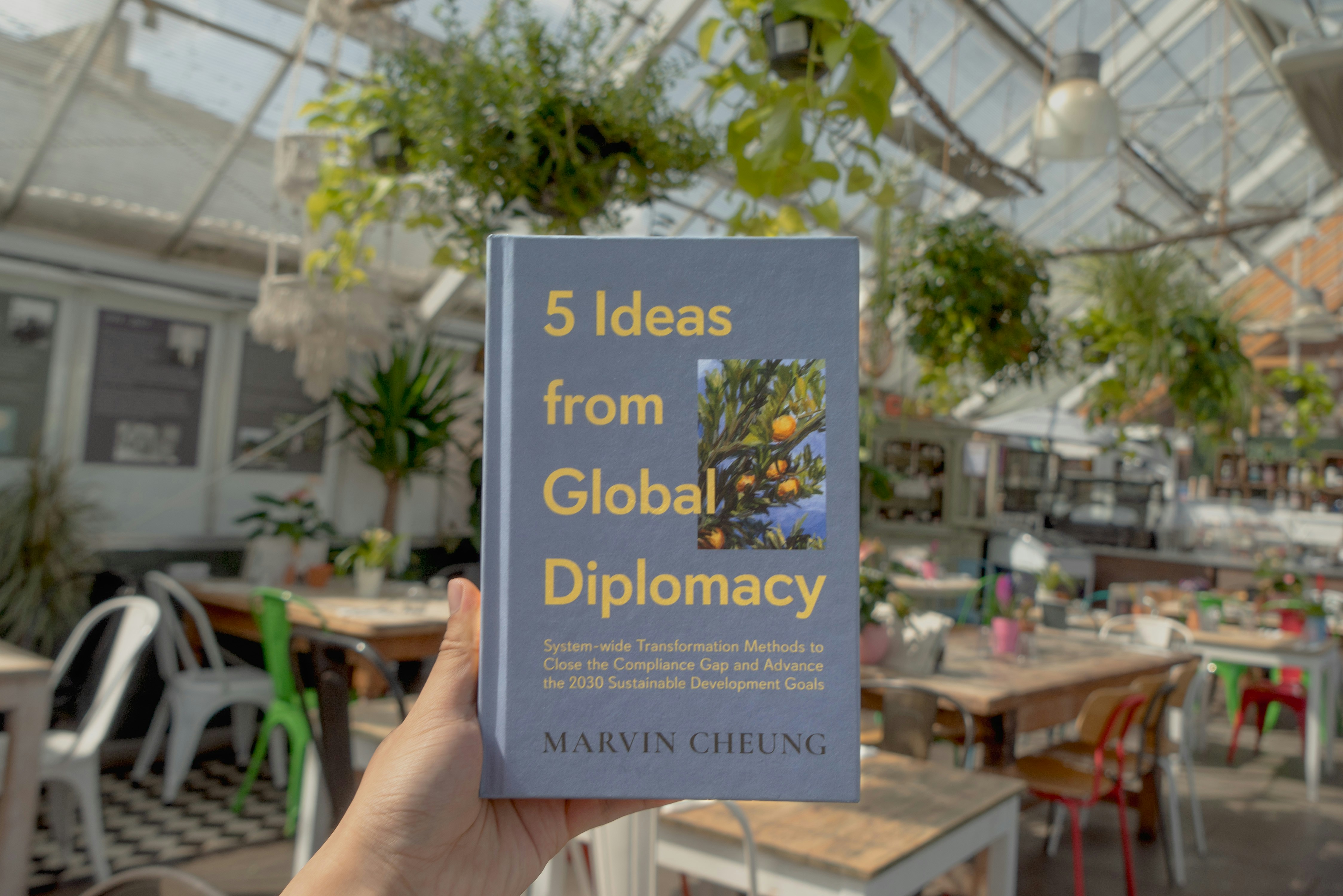 A person holding up a book in a greenhouse