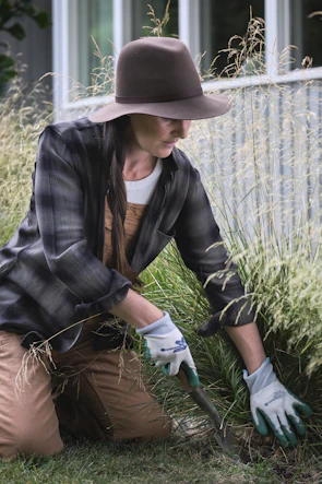 A woman in a hat and gloves working in the grass