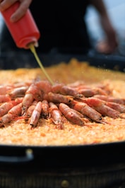 A person is pouring a sauce on a plate of cooked shrimp