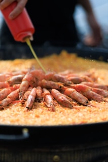 A person is pouring a sauce on a plate of cooked shrimp