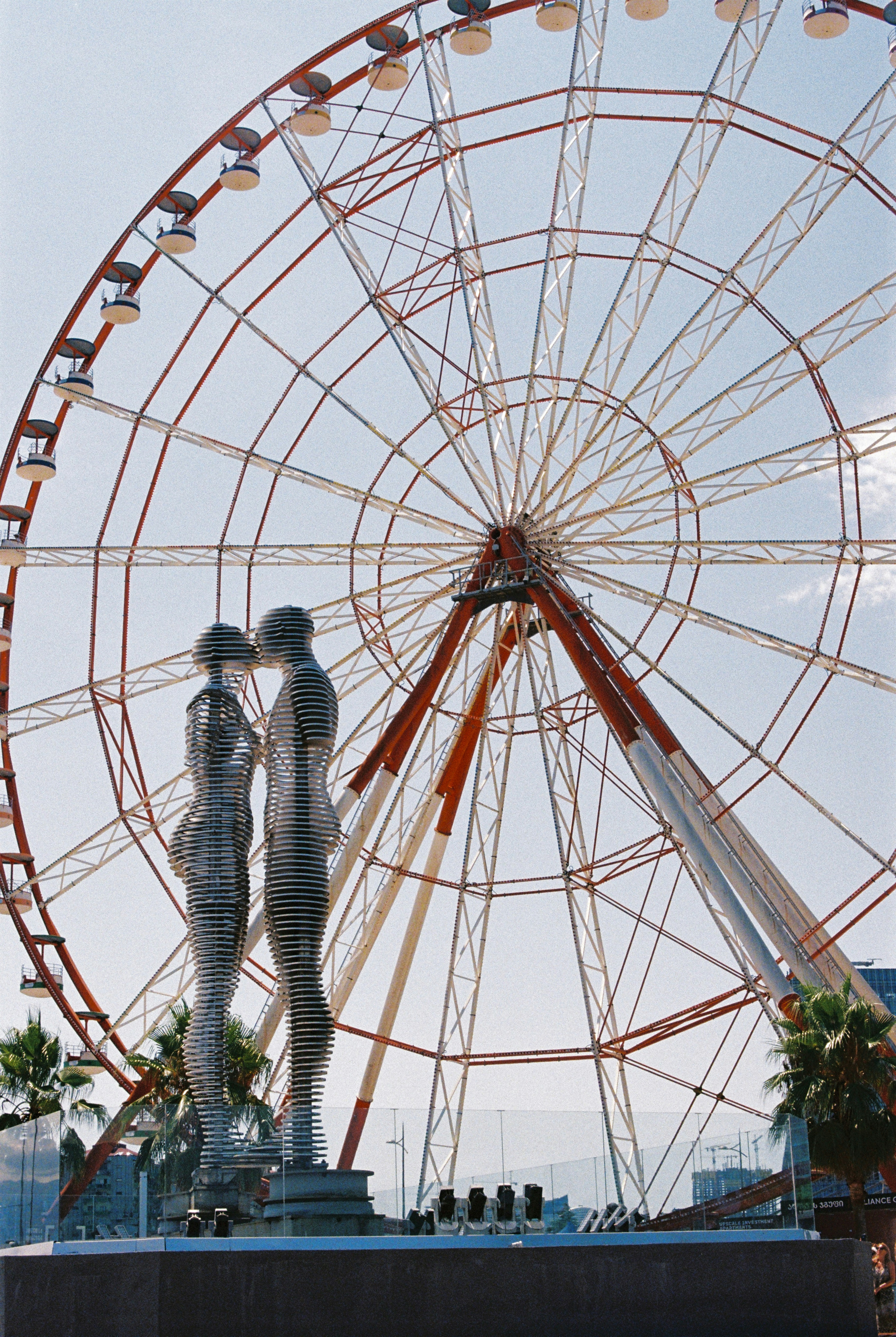 A ferris wheel with a couple kissing in front of it
