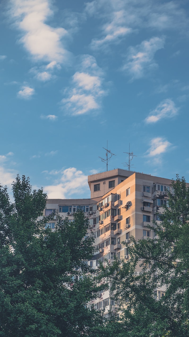 A tall apartment building surrounded by trees under a blue sky