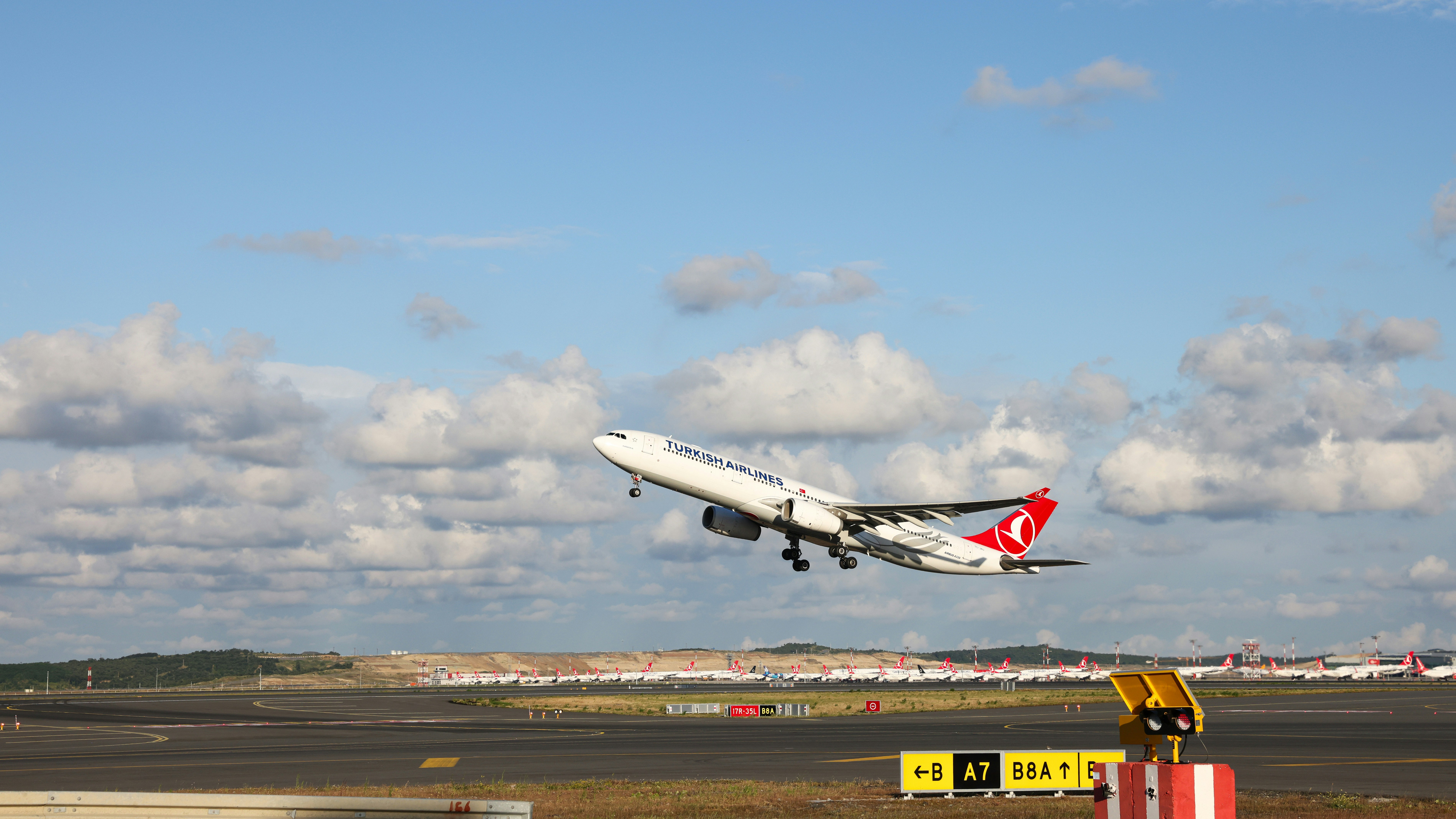 A large jetliner flying through a blue cloudy sky, Turkish Airlines Airbus A330-300 soaring against a backdrop of delicate clouds.