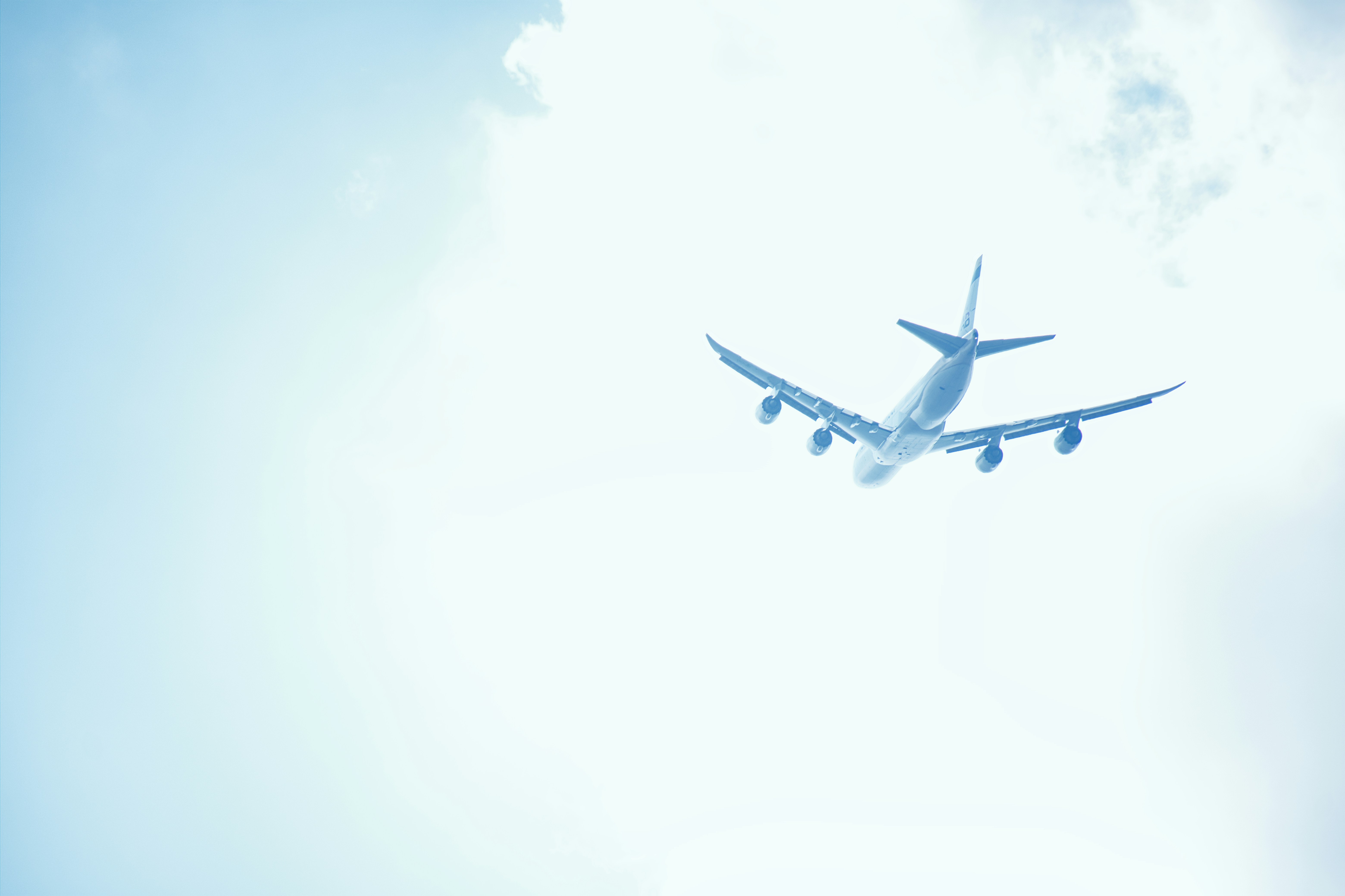 Commercial aircraft flying at high altitude with clear blue sky, deep shadow on fuselage underside, dramatic low-angle view