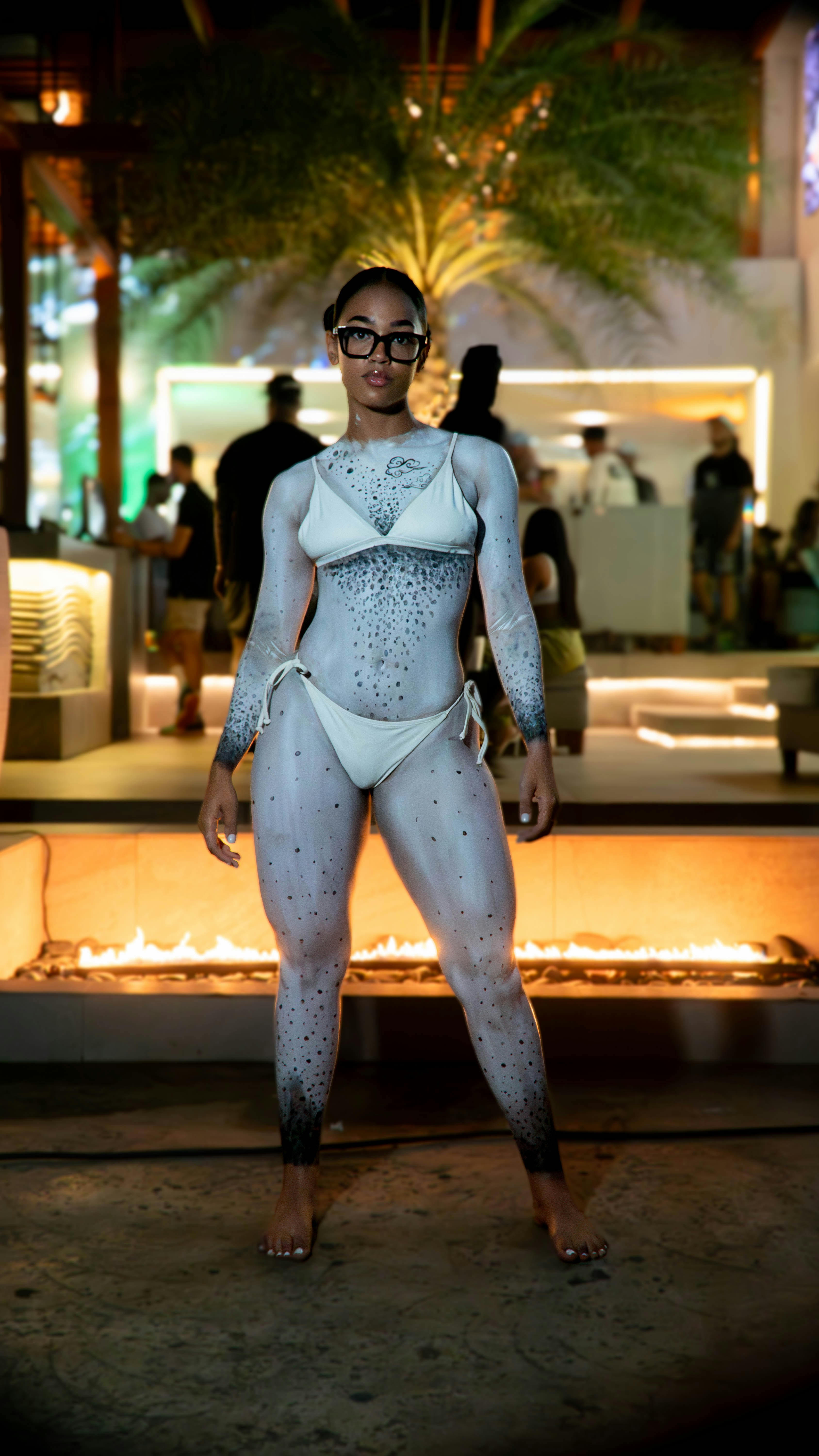 Seorang wanita dengan bodysuit putih berdiri di depan lubang api