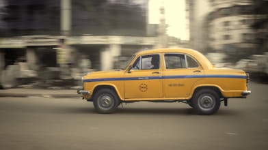A yellow car driving down a street next to tall buildings