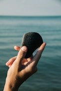 A hand holding a rock over a body of water