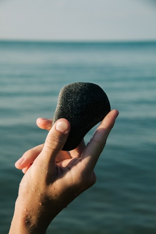 A hand holding a rock over a body of water
