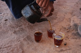 A man pours a cup of tea into two glasses
