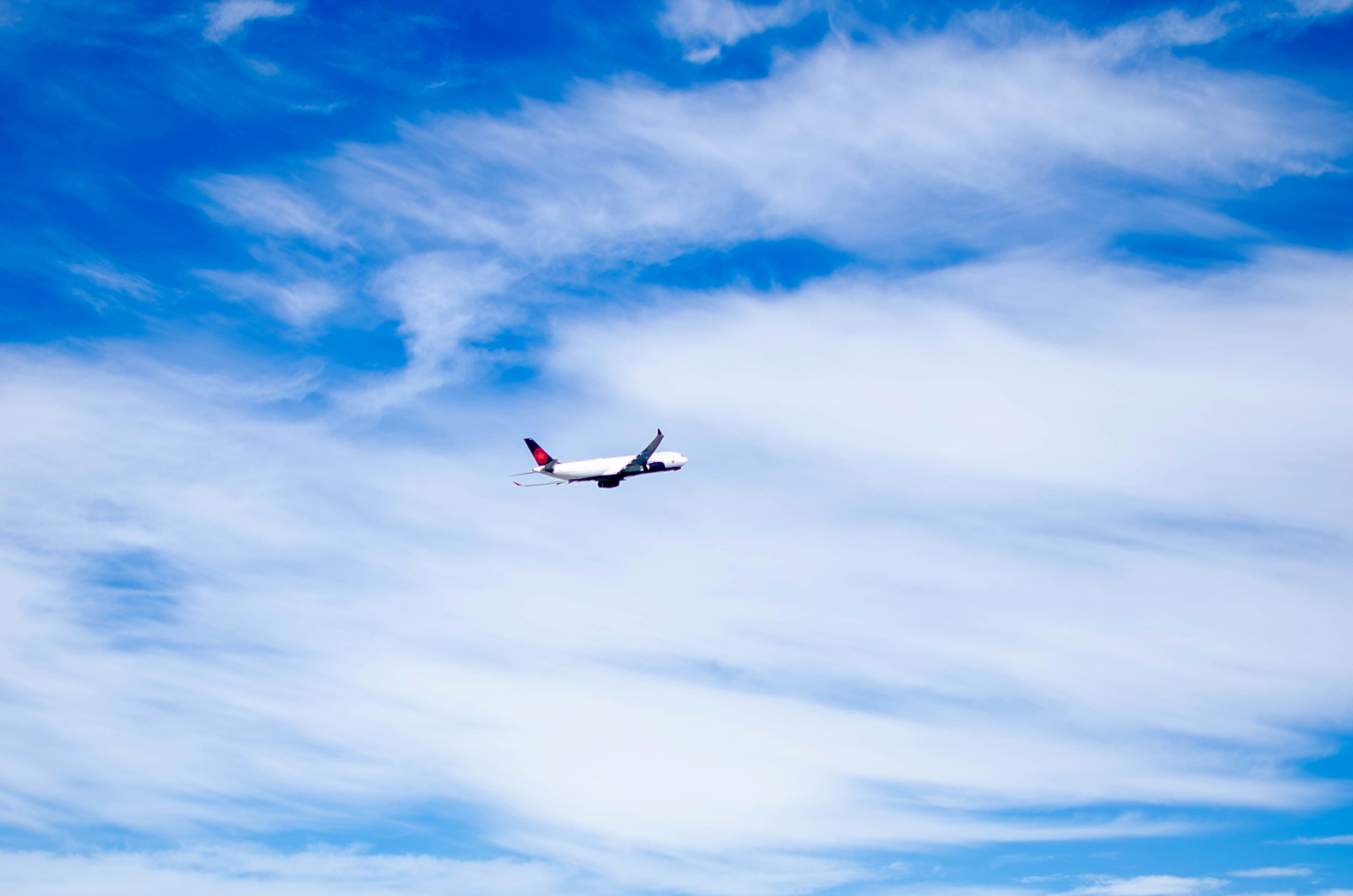 An airplane is flying in the blue sky, An Air Canada airplane soars into the sky after takeoff from YVR - Vancouver Airport. The plan is captured in mid-flight against a backdrop of vibrant blue and wispy clouds. The clean and dynamic composition highlights the vastness of the sky and the graceful movement of the aircraft, symbolizing the freedom and adventure of travel.