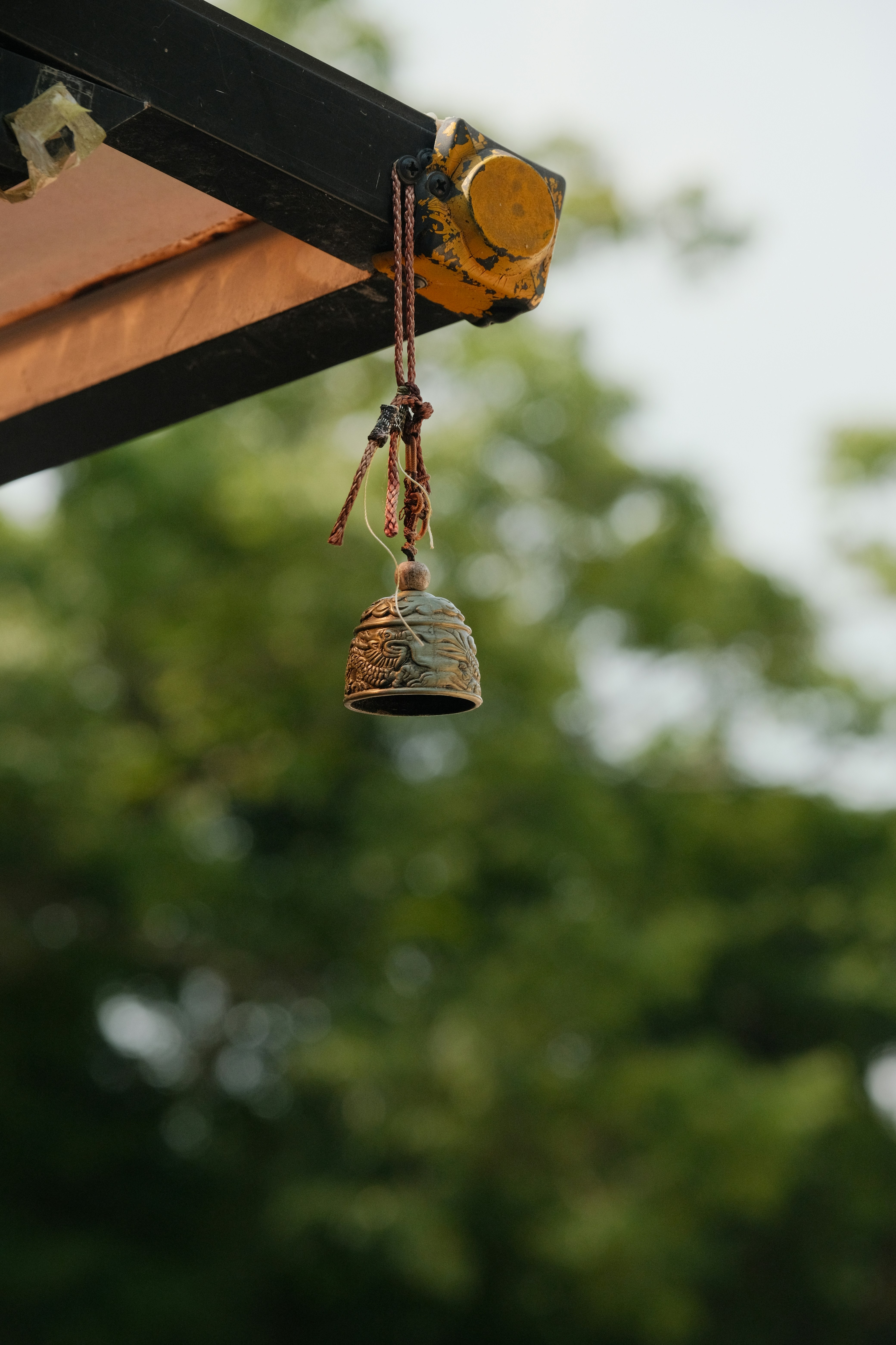 A bell hanging from a wooden structure with trees in the background