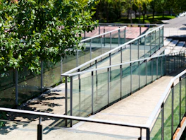 A tennis court with glass railings and trees