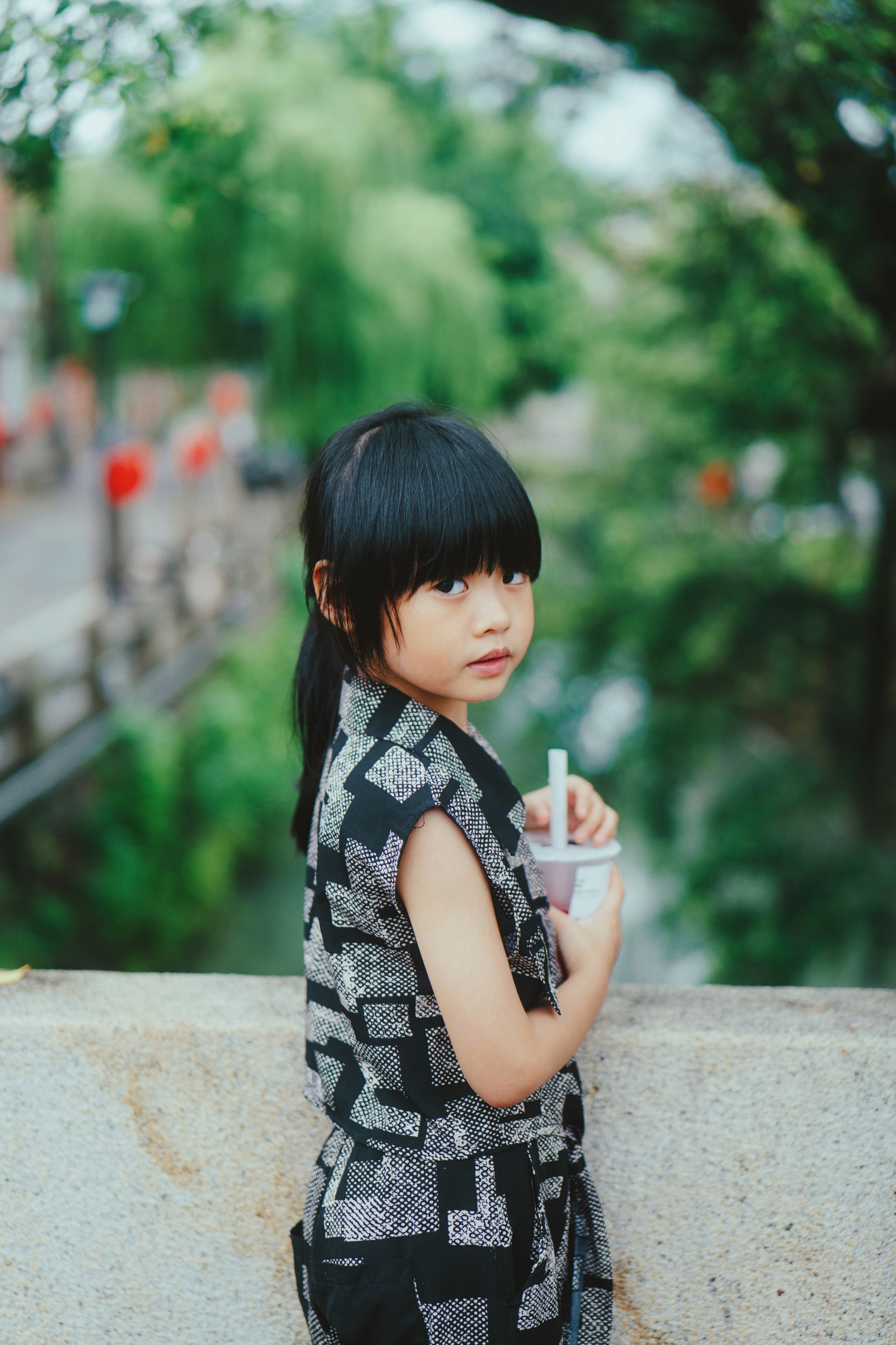 A little girl standing on a ledge holding a cup