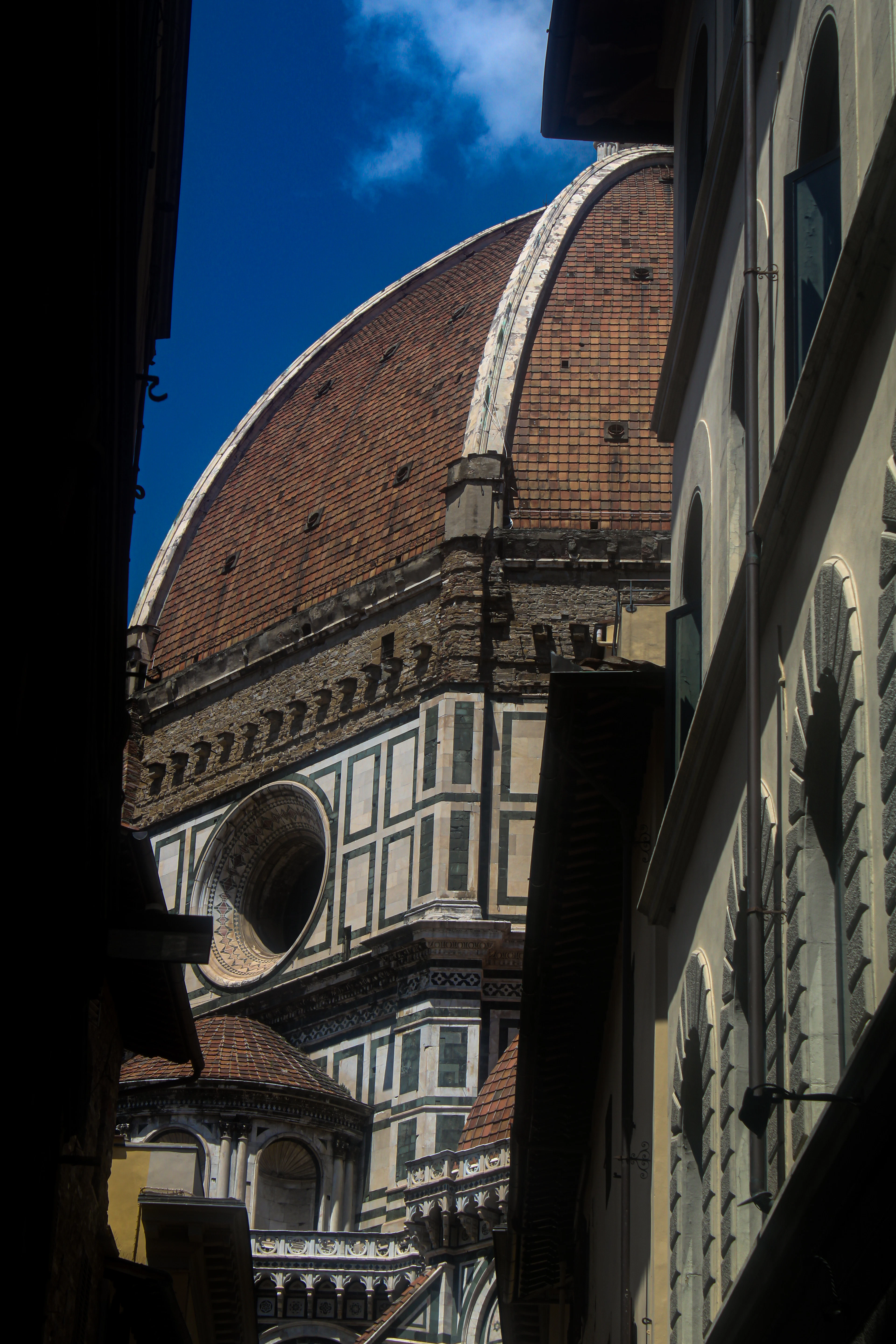 The green-and-white marble flank of Florence cathedral seen from a narrow street below