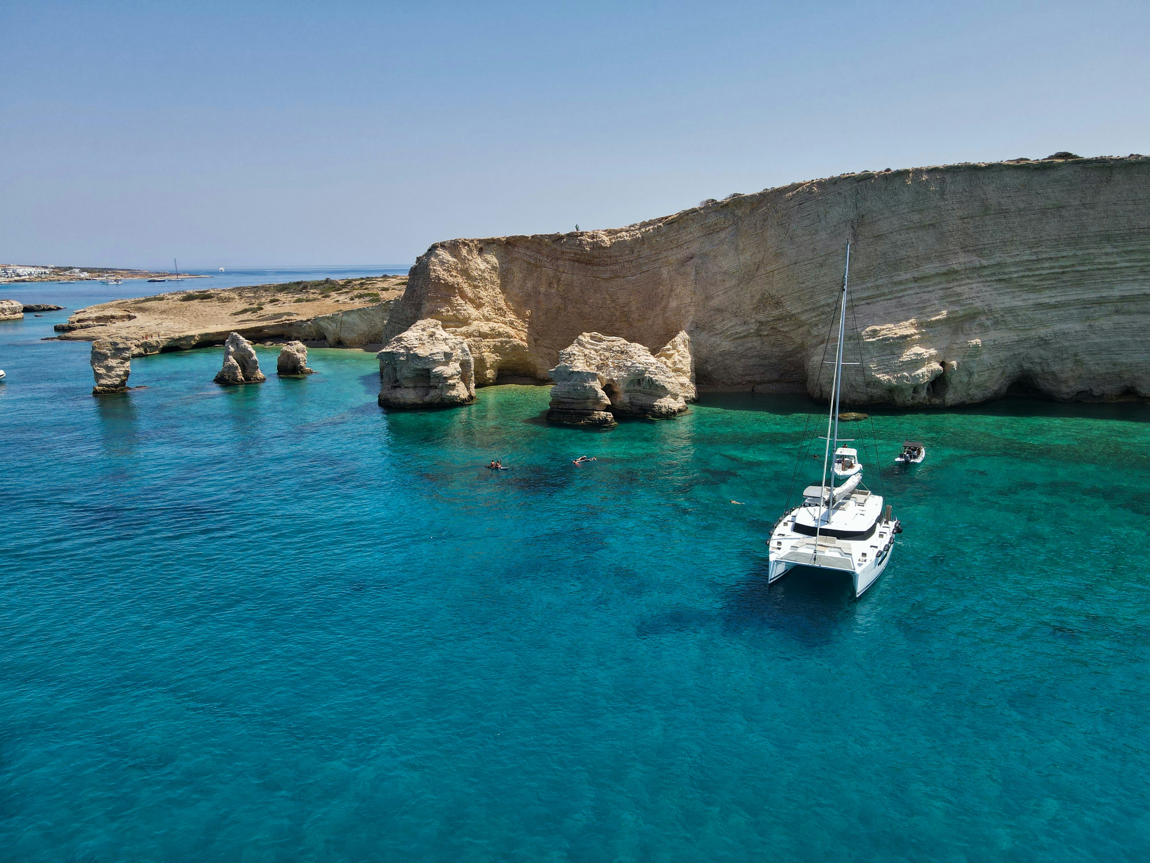 A white boat floating in the ocean next to a rocky cliff