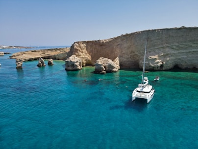 A white boat floating in the ocean next to a rocky cliff