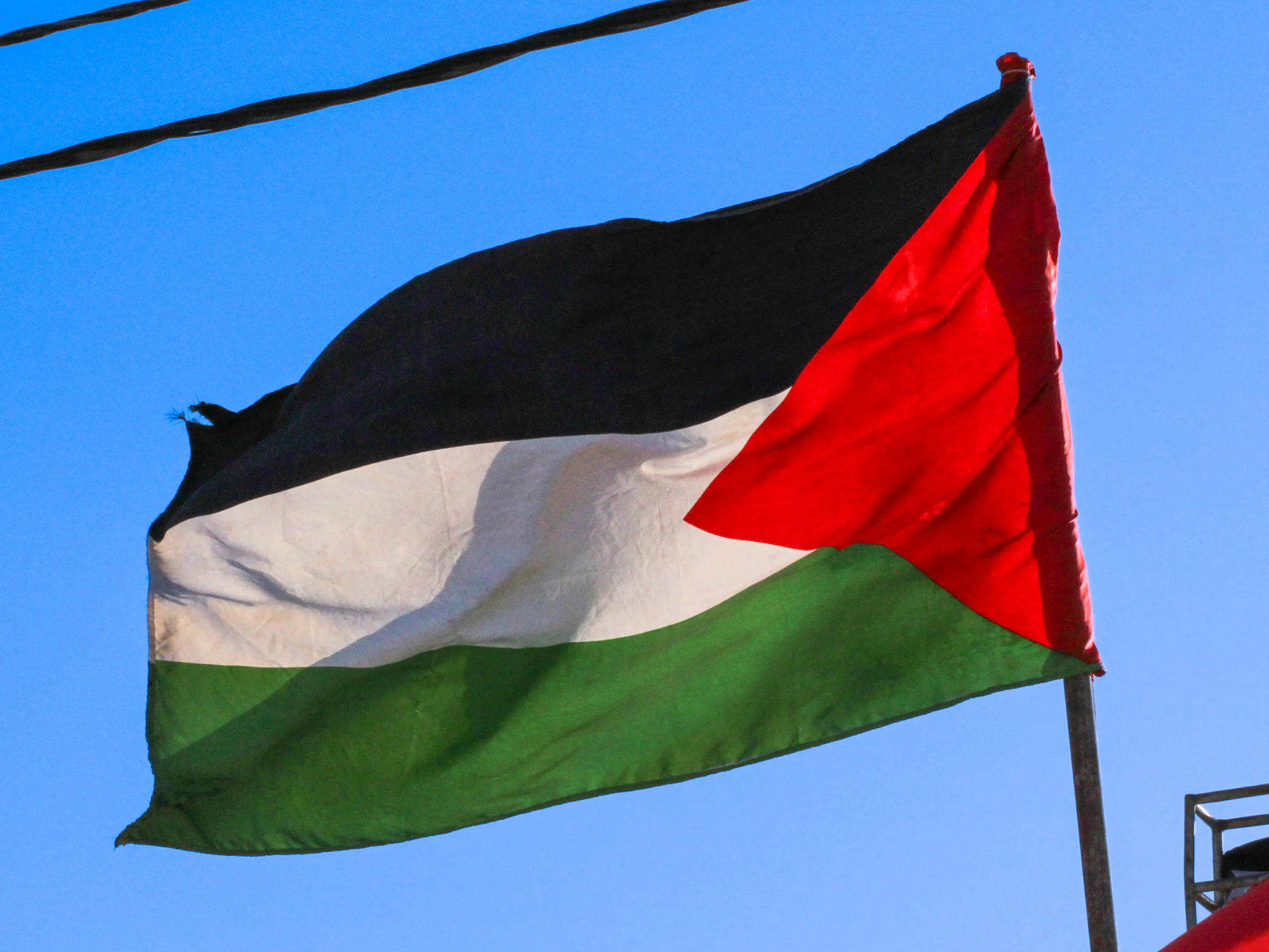 A Palestinian flag flying from a pole against a clear blue sky