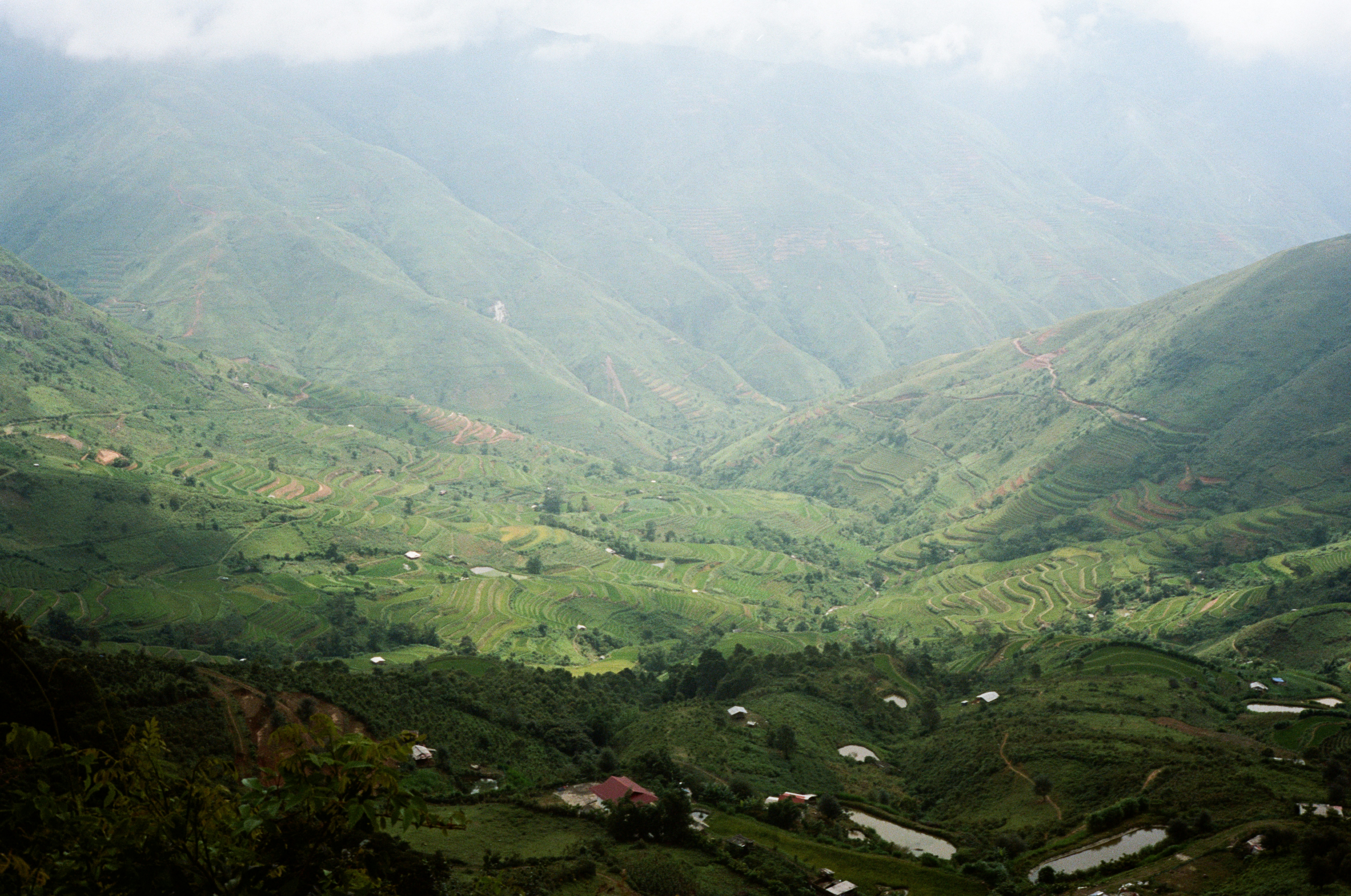 Remote mountain valley with terraced hillsides, misty morning atmosphere, deep shadows, lush greenery