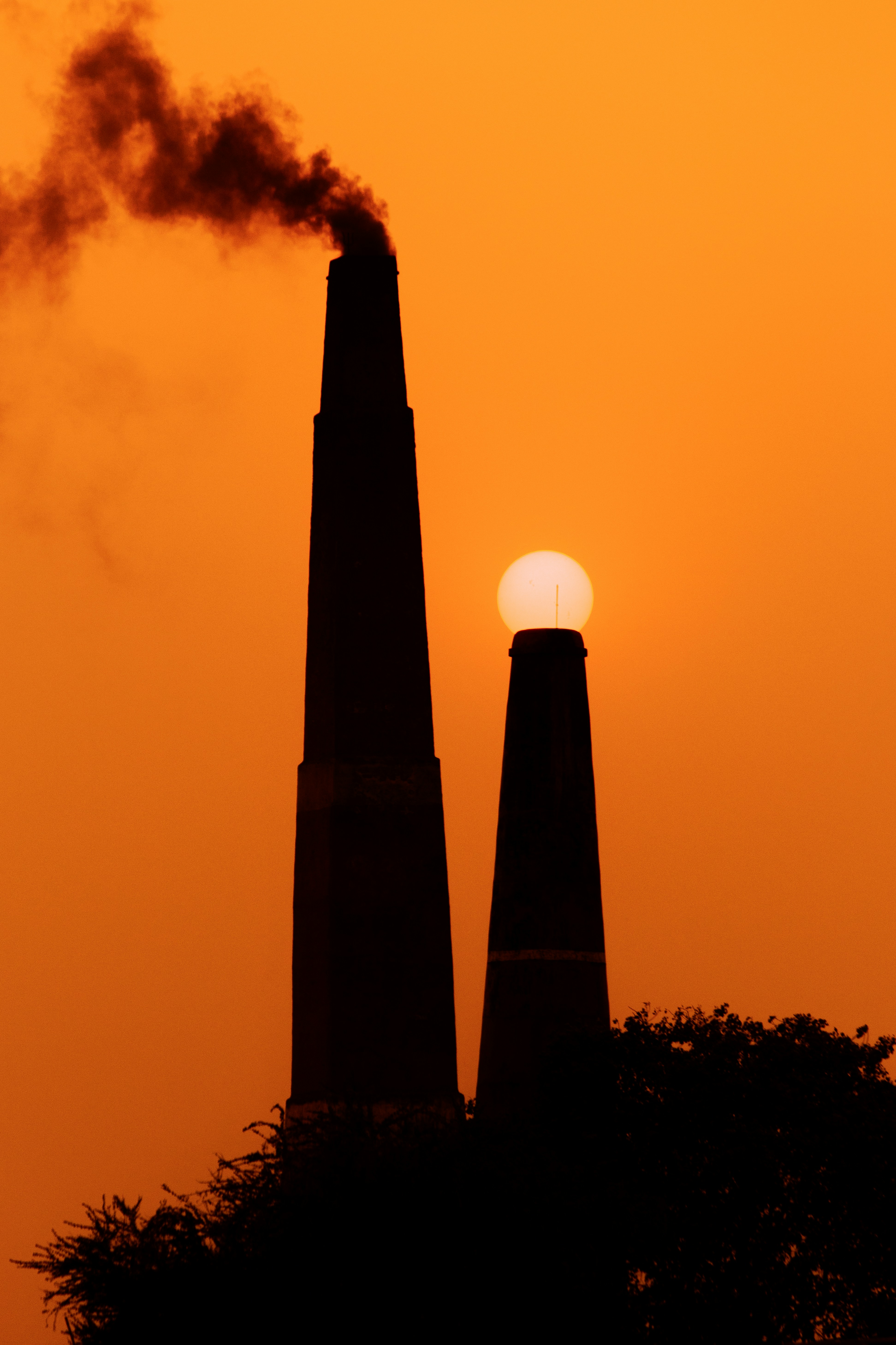 The sun is setting behind two smoke stacks