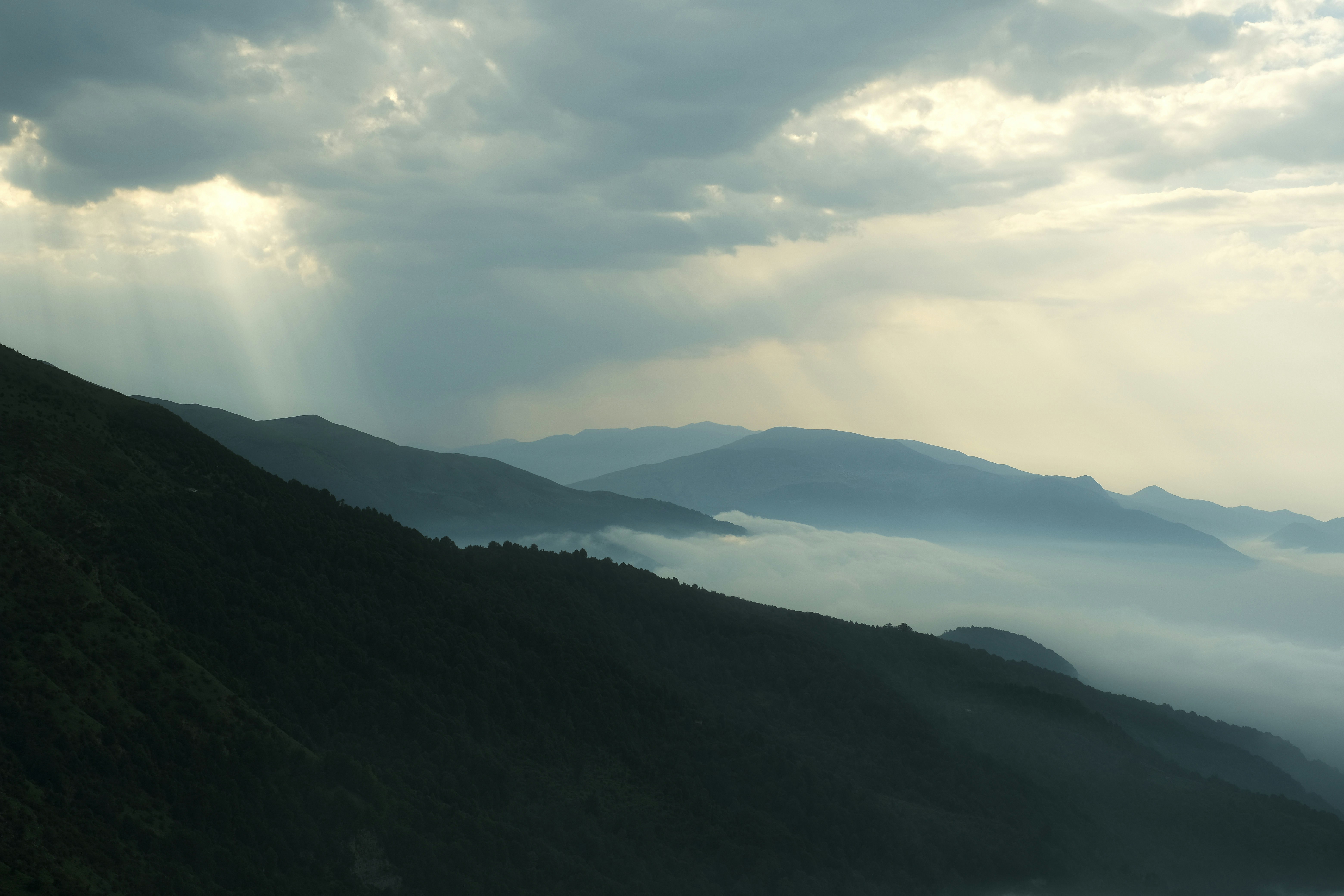 The sun shines through the clouds over the mountains