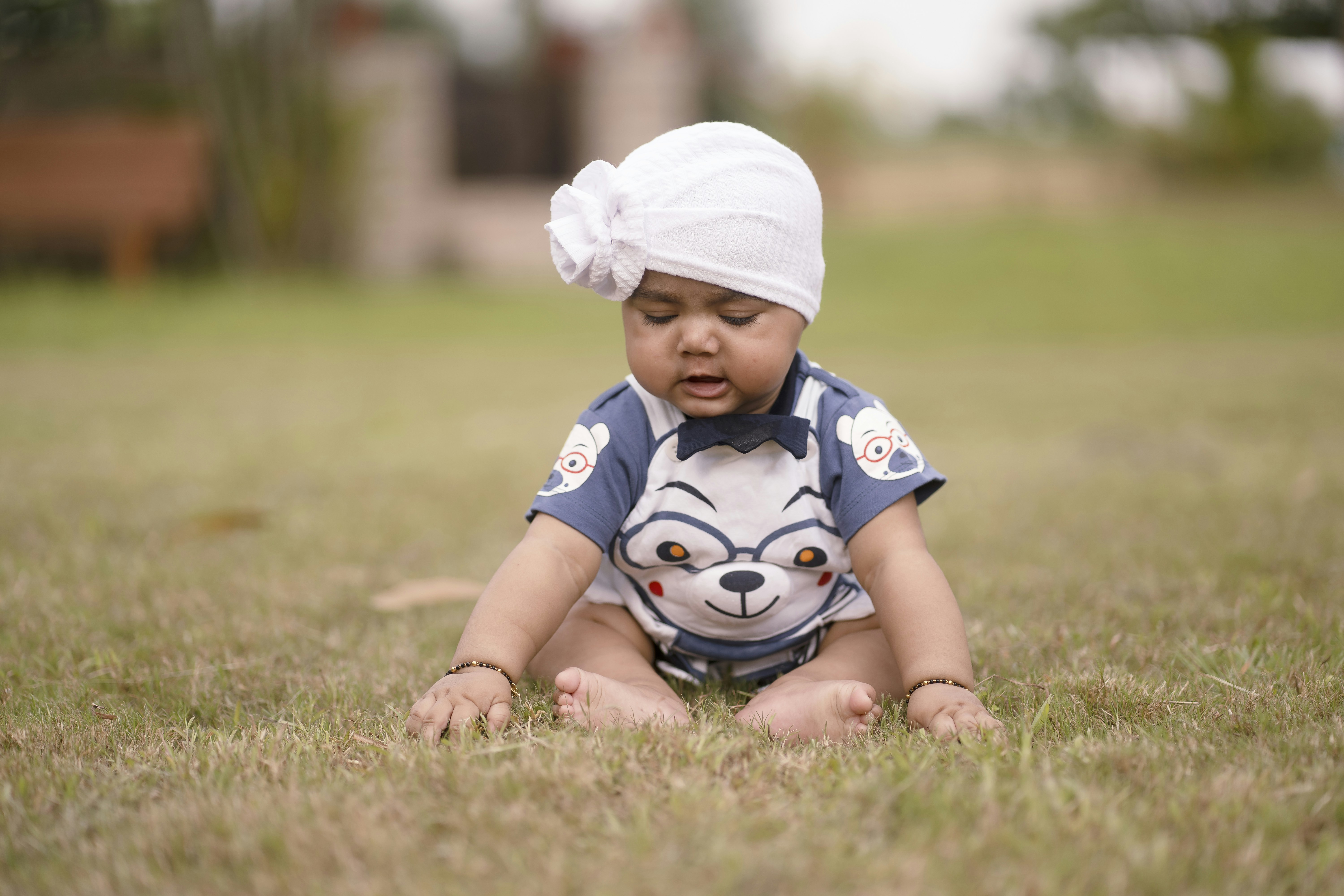 Seorang bayi duduk di rumput mengenakan topi putih