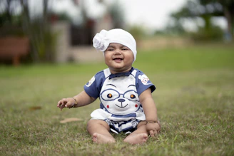A baby sitting in the grass wearing a turban