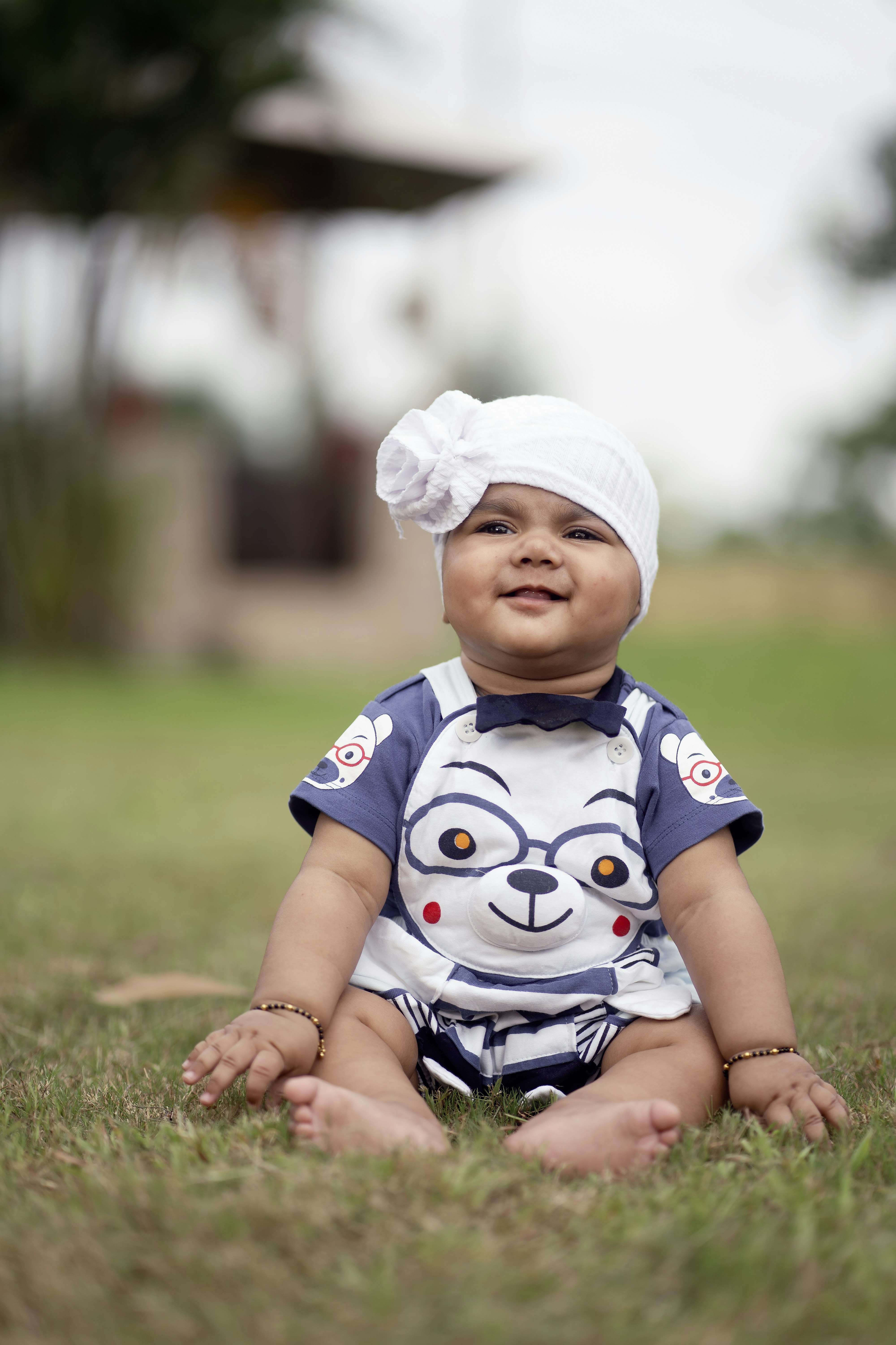 Seorang bayi duduk di rumput mengenakan topi