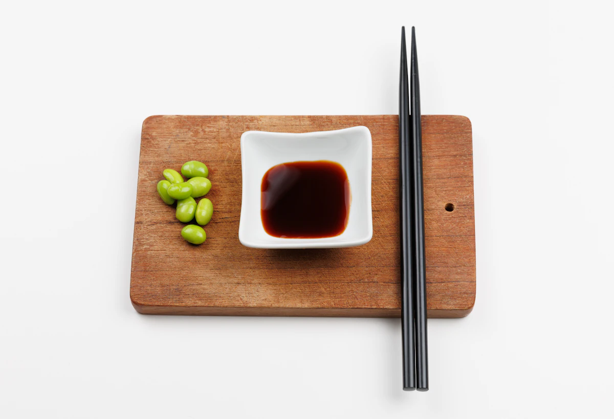 A chopping board with chopsticks and a small bowl of sauce