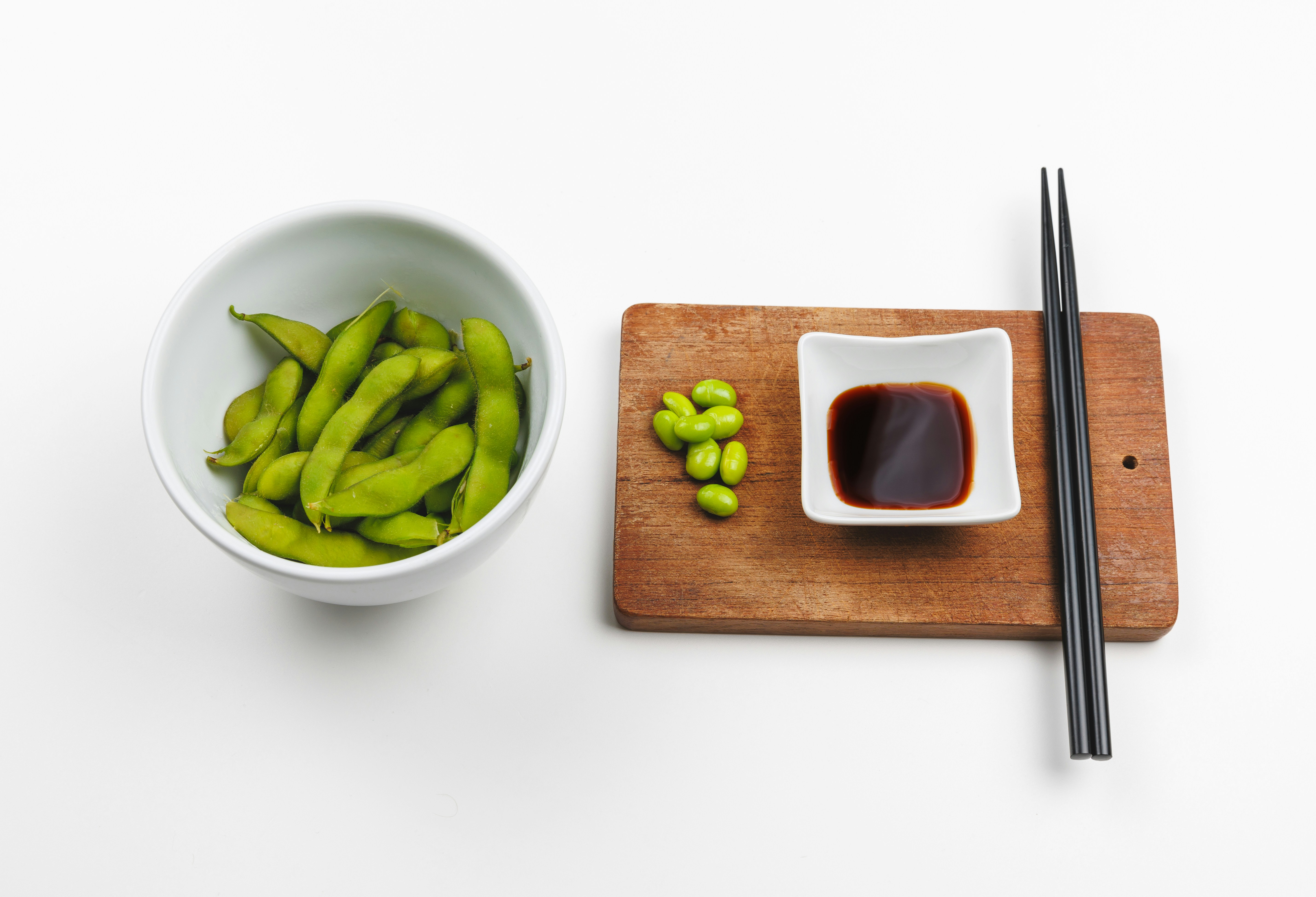 A chopping board with chopsticks and a bowl of green beans
