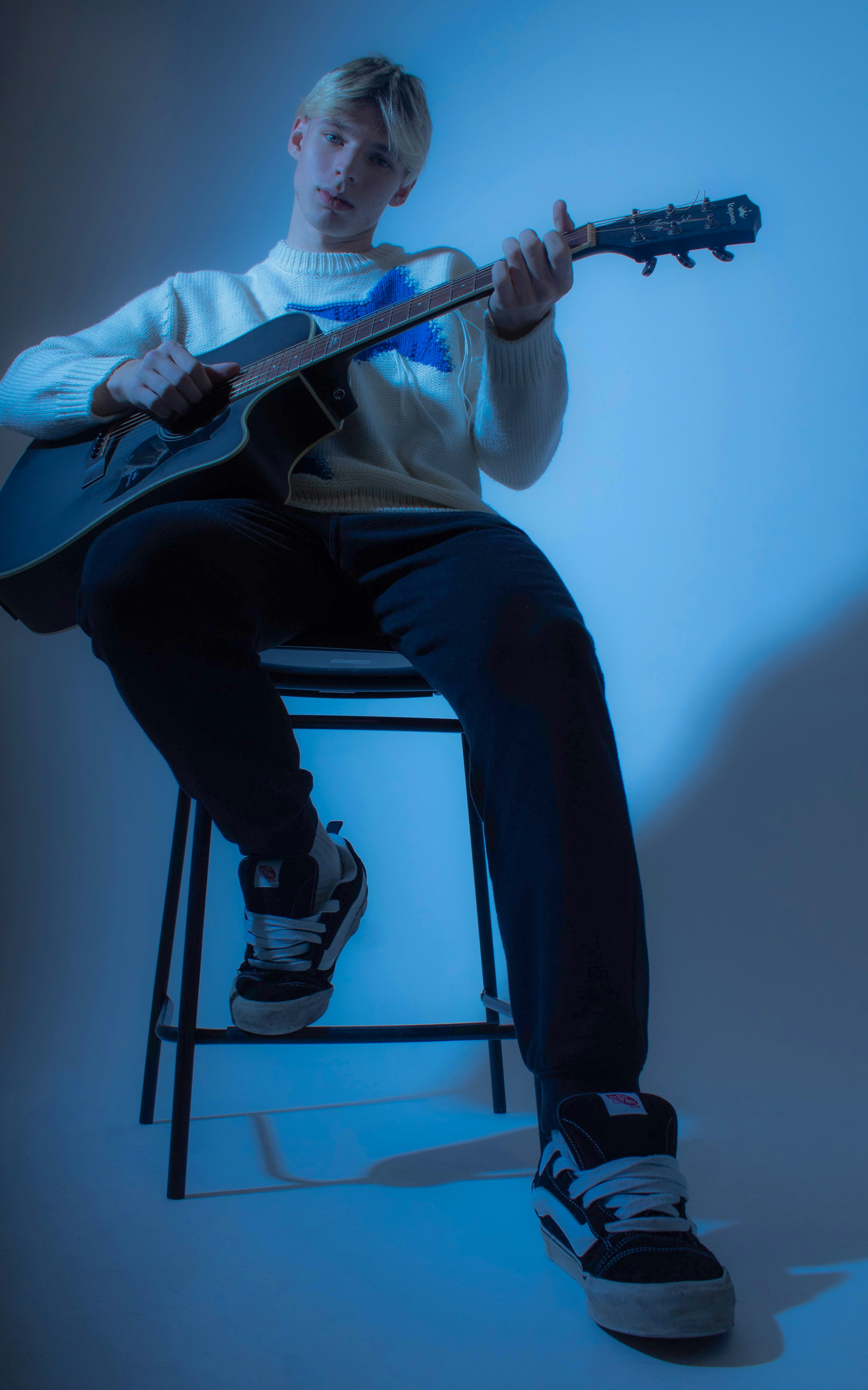 Ein Mann sitzt auf einem Hocker und hält eine Gitarre in der Hand