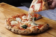 A person taking a slice of pizza from a wooden cutting board