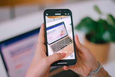 A person holding a cell phone in front of a laptop