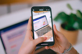 A person holding a cell phone in front of a laptop