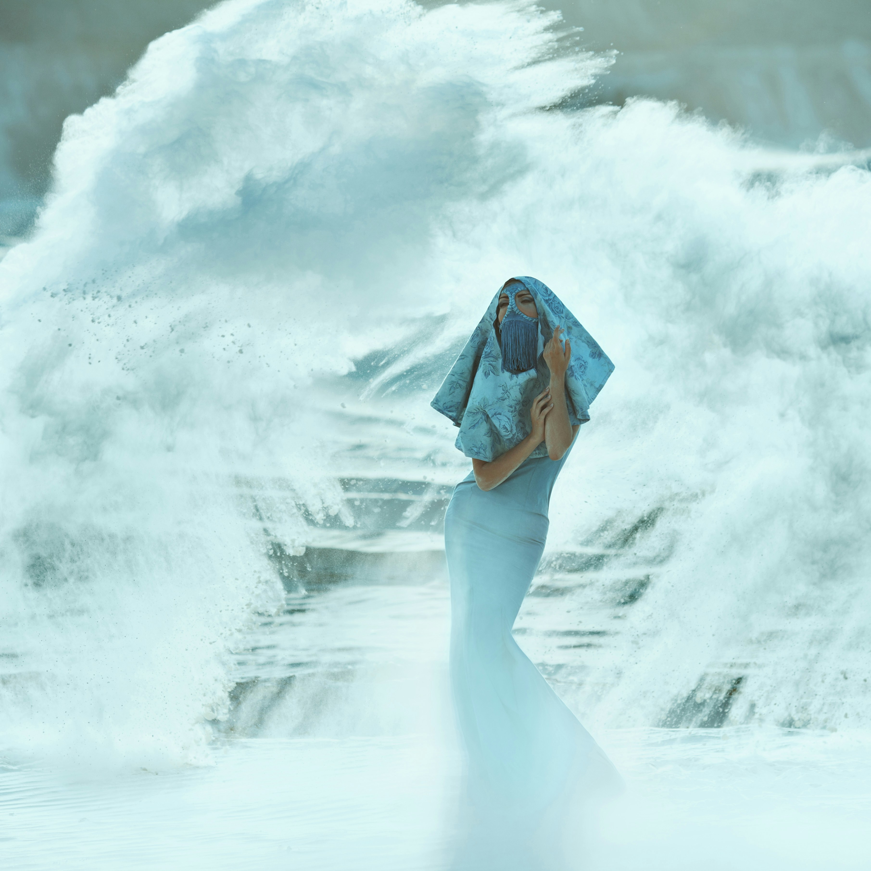 A woman in a blue dress standing in front of a large wave