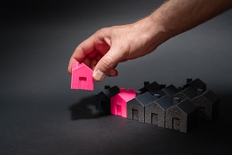 A hand reaching for a pink house in front of a row of houses