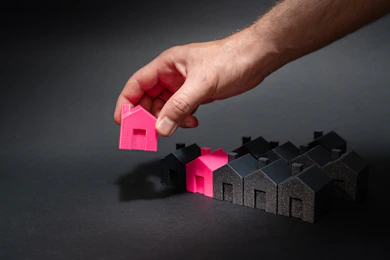 A hand reaching for a pink house in front of a row of houses