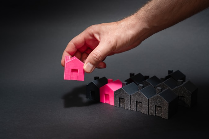 A hand reaching toward one home among a row of houses, representing a buyer choosing from available Clark County inventory
