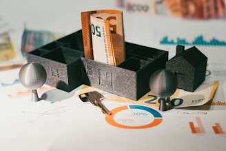 Miniatura de casa sobre notas e moedas representando planejamento financeiro e impostos.