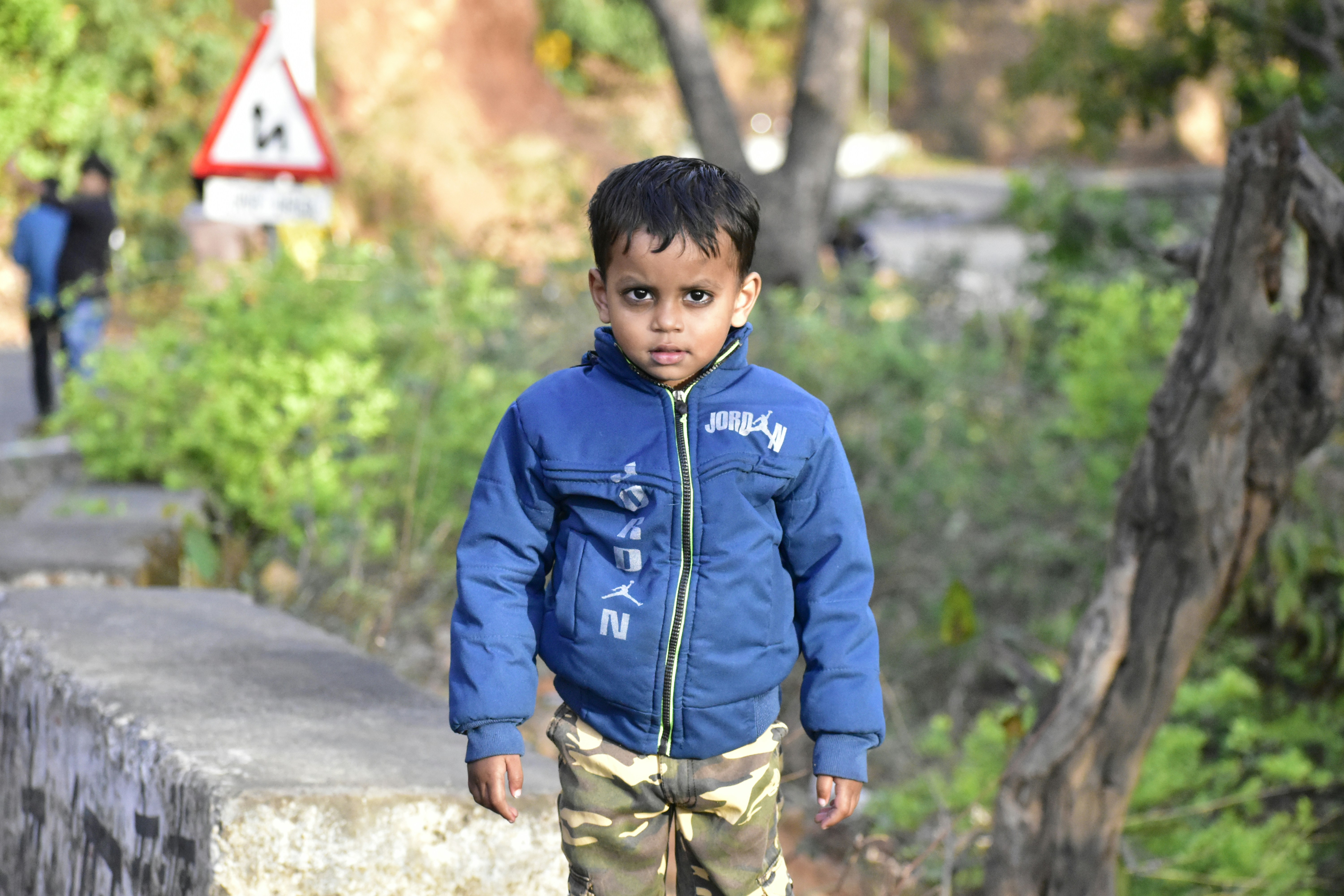 A young boy walking down a sidewalk next to a forest