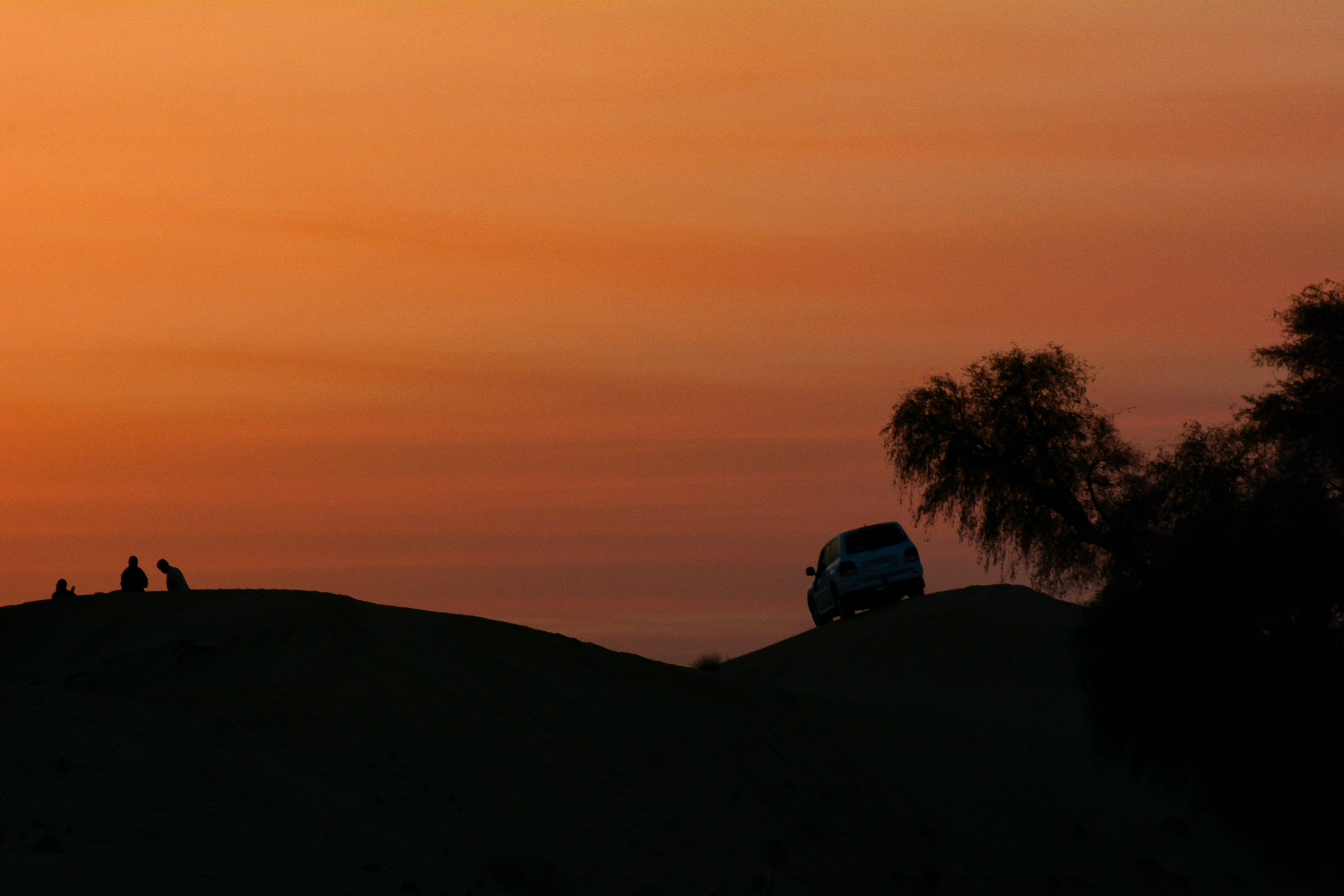The sun is setting over a hill with people sitting on it