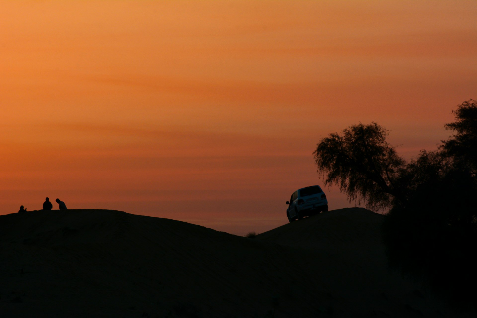 The sun is setting over a hill with people sitting on it