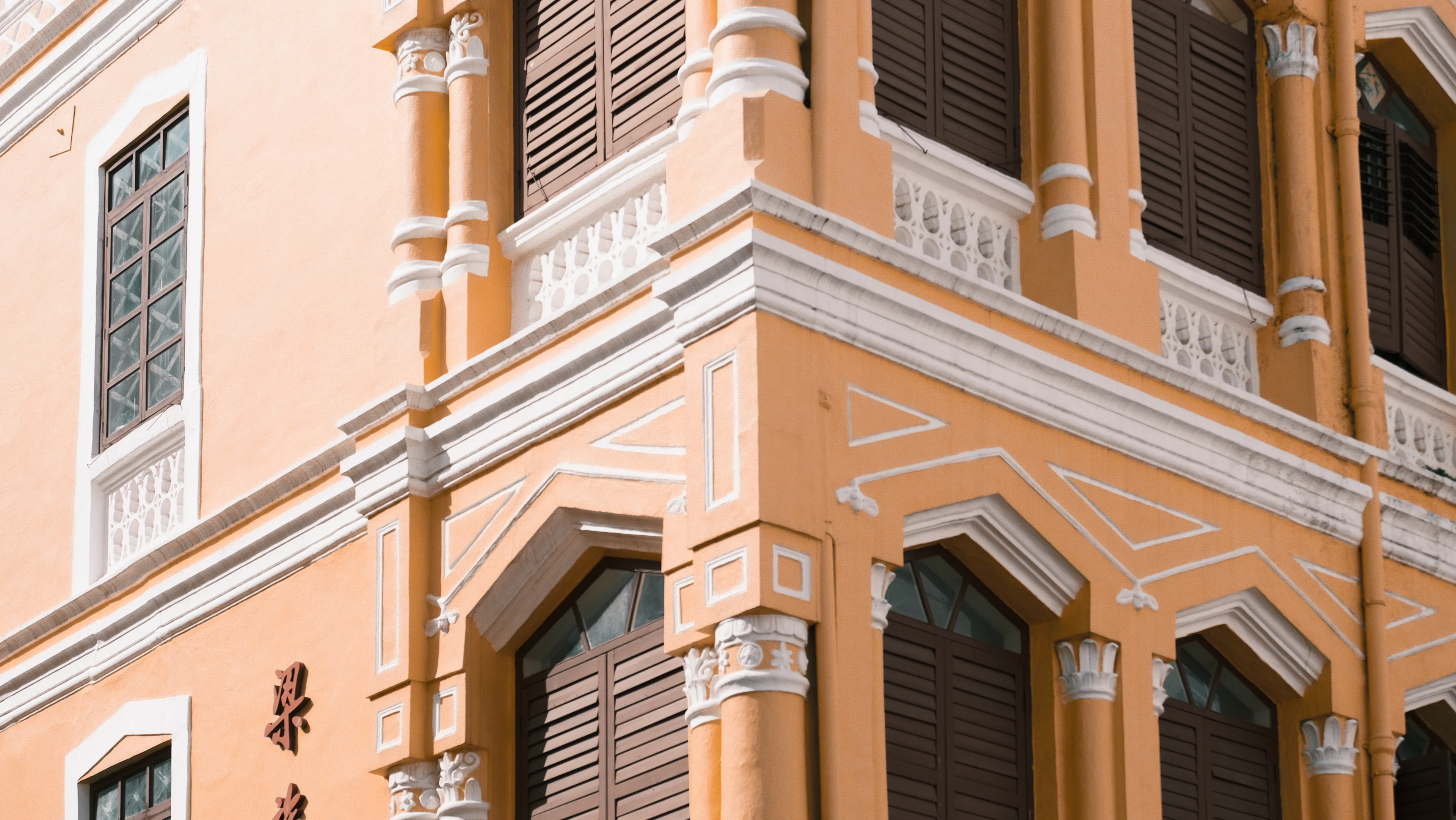 Close-up corner of an ochre colonial building with white stucco trim and dark shutters in warm sunlight.