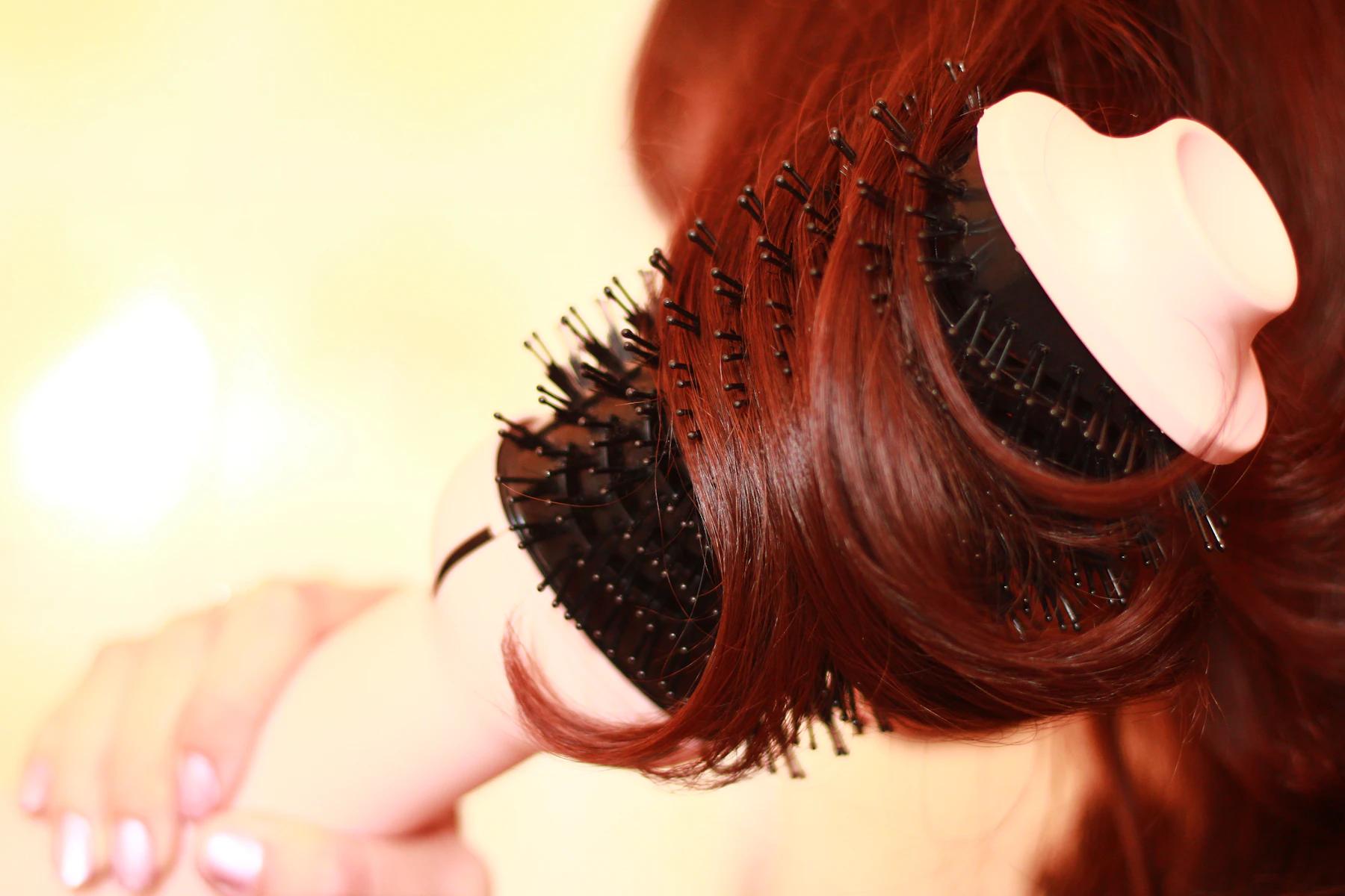 Close on a round brush rolled into copper hair during a blow-dry