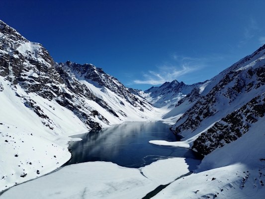 The Laguna del Inca half-frozen between steep snowy Andean walls under a blue sky at Portillo