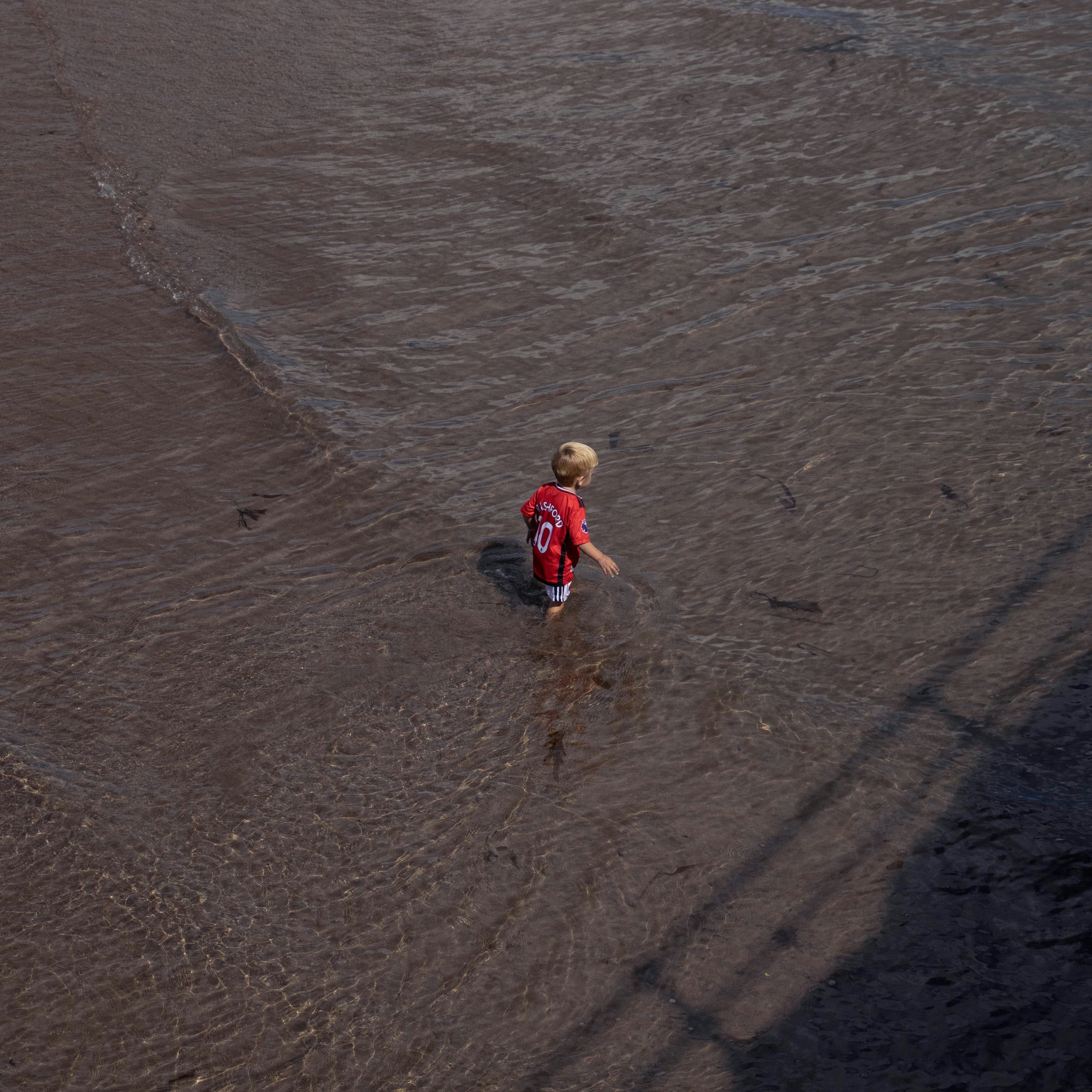 A young boy wading in the water near a bridge