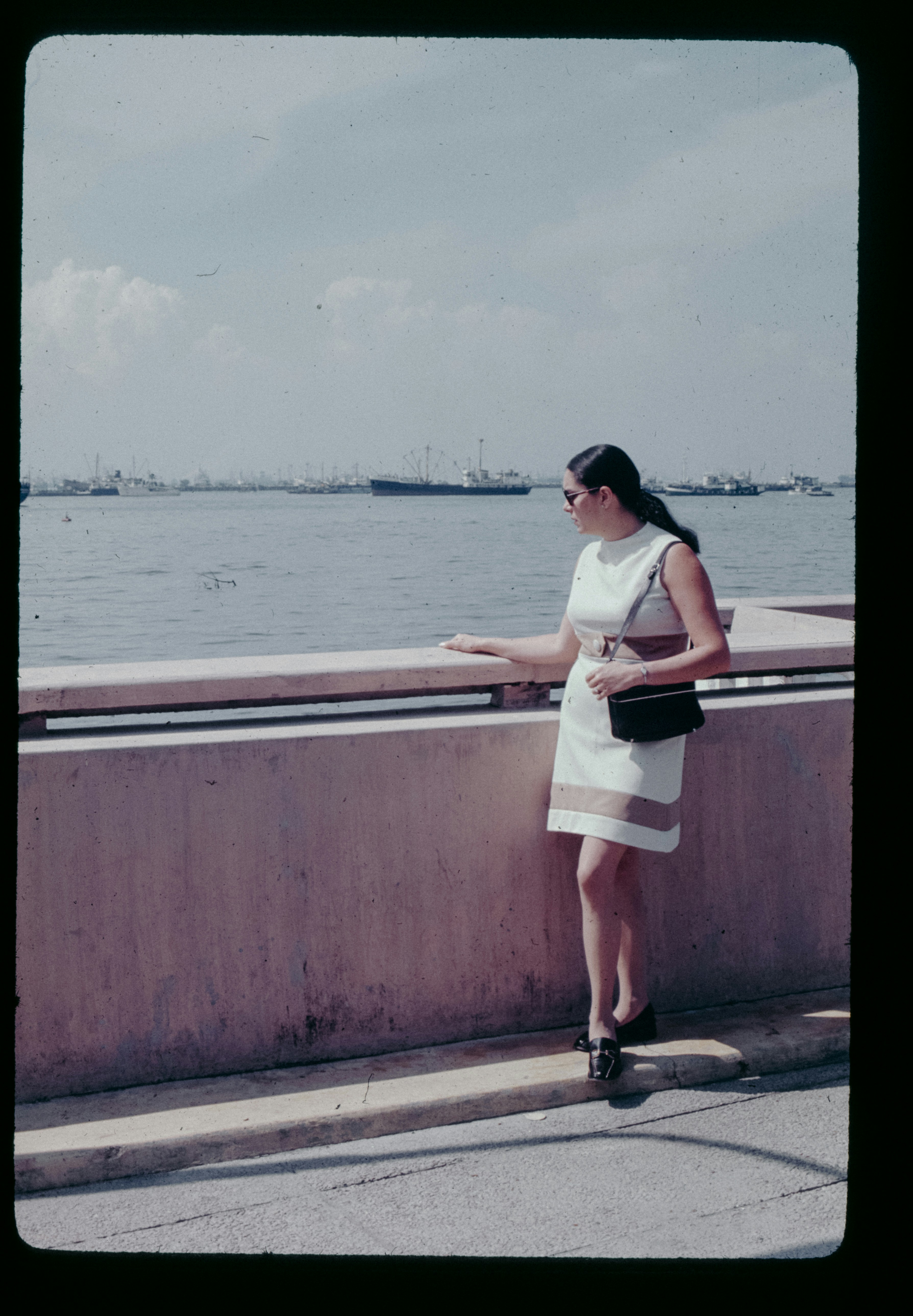 A woman in a white dress standing on a bridge next to a body of water ...