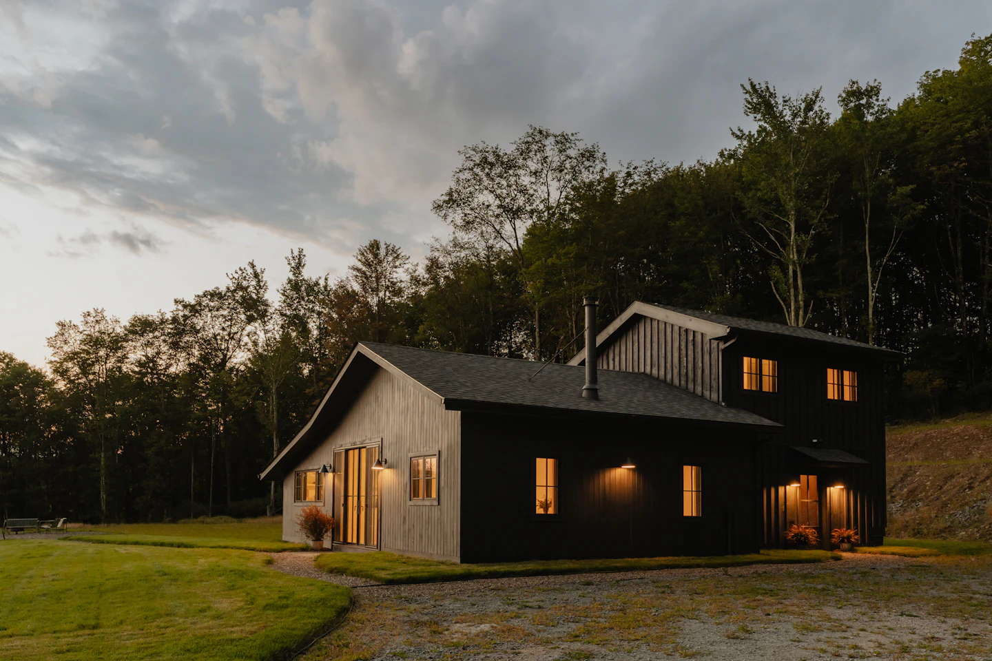 Black modern farmhouse on a green lawn at dusk